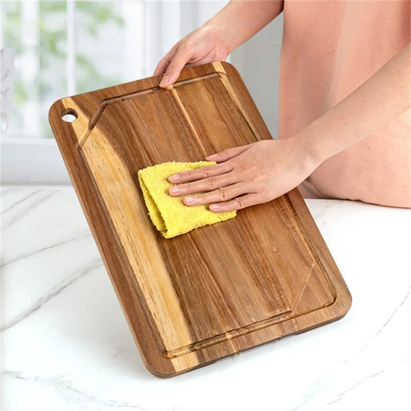 Person cleaning a acacia wooden cutting board with a yellow cloth on a white surface.