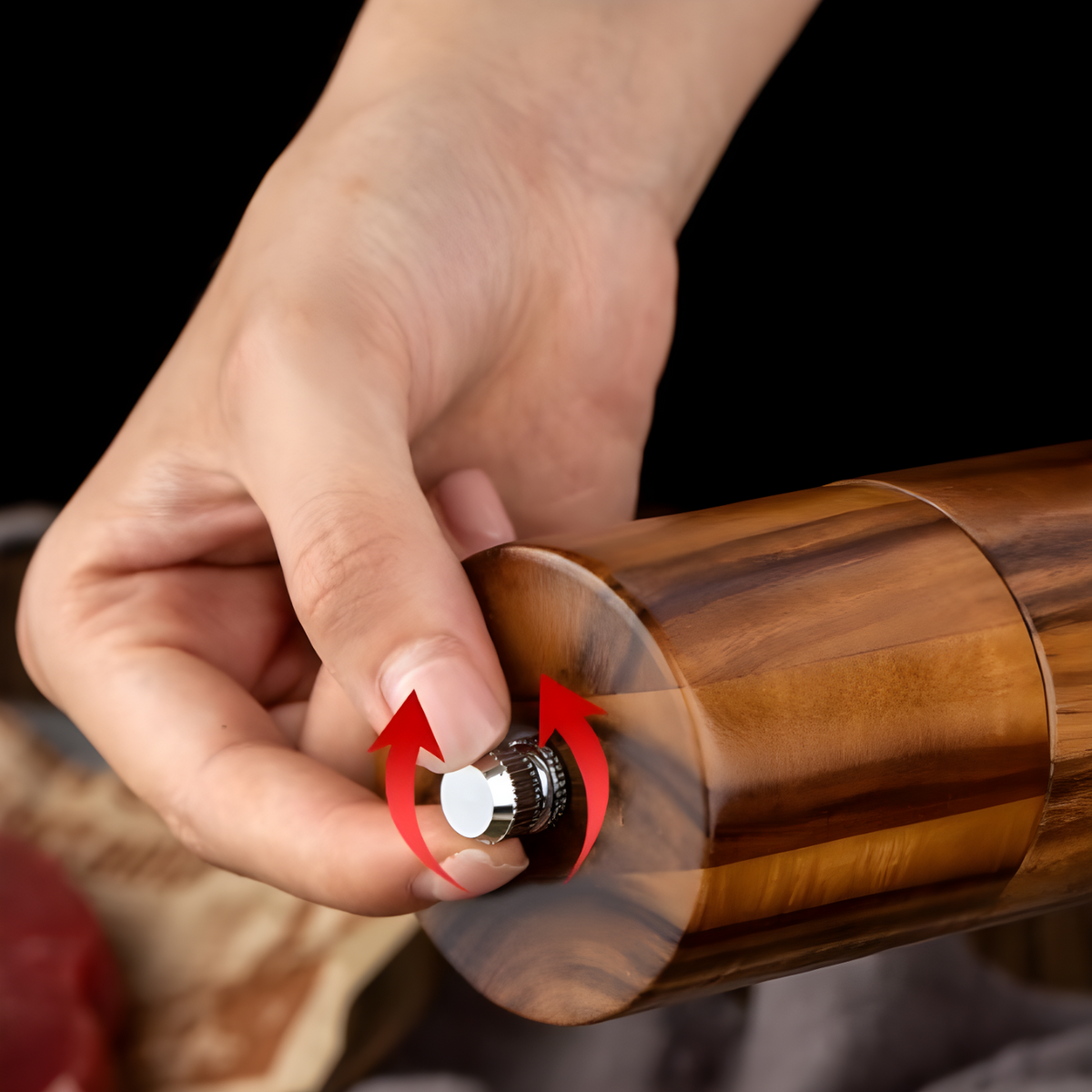 A close-up of a hand holding the accacia wood grinder and turning a the knob, to adjust the grinding. 