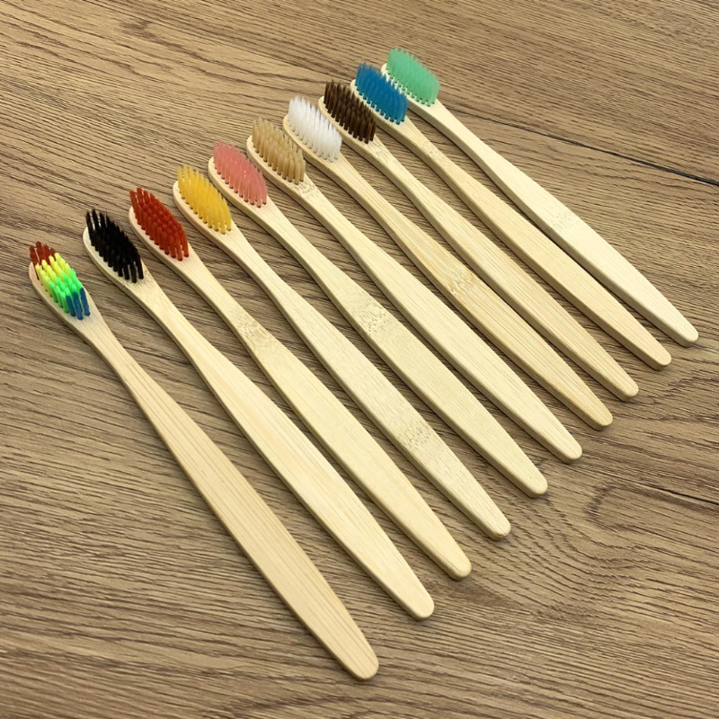 Set of bamboo toothbrushes with colored bristles on a wooden surface