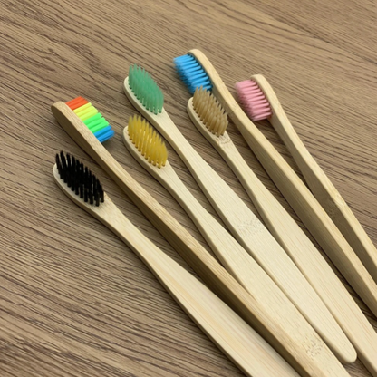 Set of bamboo toothbrushes with colored bristle heads on a wooden surface