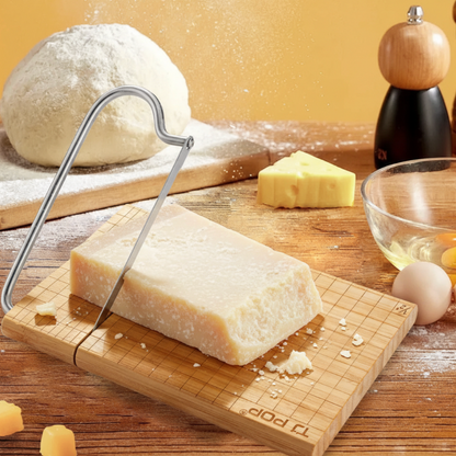 Block of cheese on a wooden board with a cheese slicer, surrounded by kitchen items.