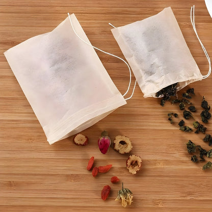Two biodegradable drawstring tea bags on a bamboo wood surface, one open and spilling dried goji berries, rose buds and rolled oolong tea leaves.