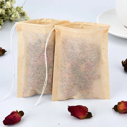 Two empty biodegradable tea bags with loose tea leaves on a light surface with dried flowers.