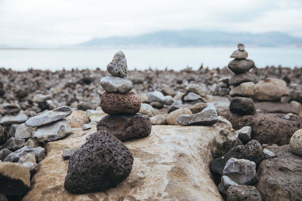 Two stone stacks on a rocky beach with a cloudy sky.