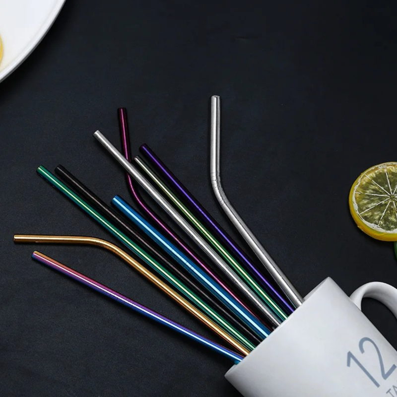 Set of colorful metal straws on a dark surface with a white mug and lemon slice.