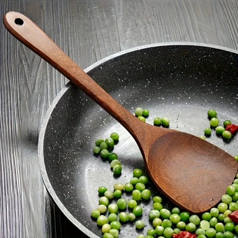 Wooden spoon in a pan with peas and red peppers on a wooden surface