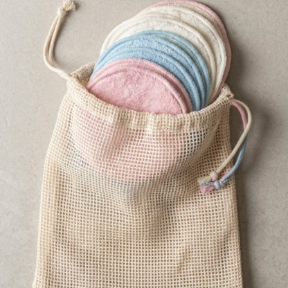Reusable bamboo fibre pads in pink, blue, and white stacked inside an open cotton mesh washing bag, top view.