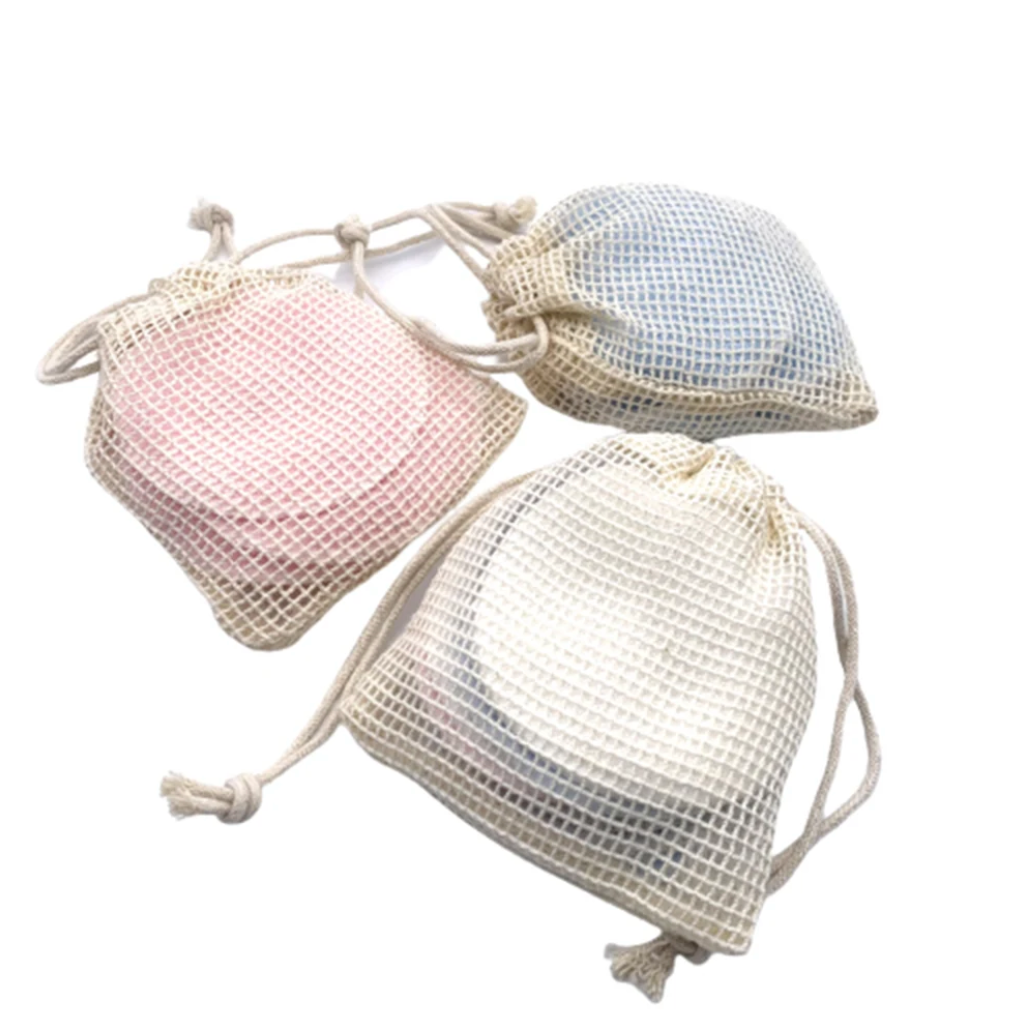 Reusable bamboo fibre pads stored inside a cotton mesh washing bag on a white background.