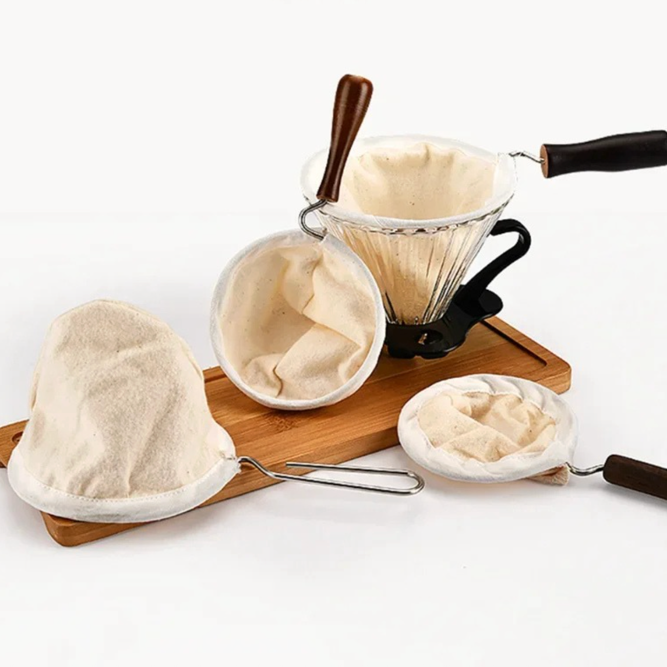 Reusable cloth coffee filters and a glass pour-over dripper arranged on a wooden board, showing the filter cone shape and accessories