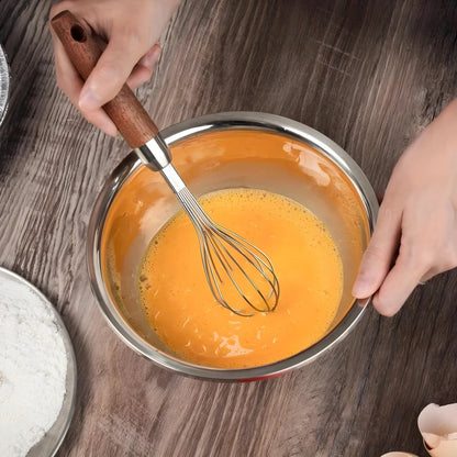 Hardwood handle whisk mixing batter in a stainless steel bowl on a wooden table