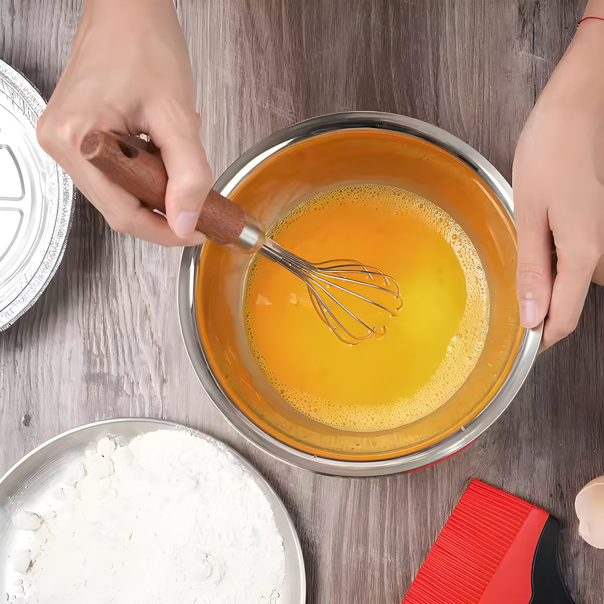 Overhead view of a hardwood handle whisk beating egg yolk in a white bowl