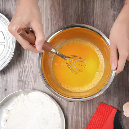 Overhead view of a hardwood handle whisk beating egg yolk in a white bowl