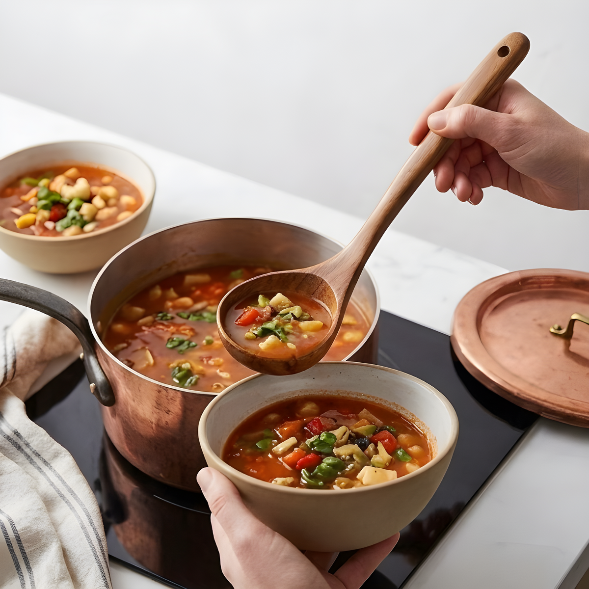 Hand using a teak soup ladle to serve vegetable minestrone from a copper pot into a ceramic bowl.